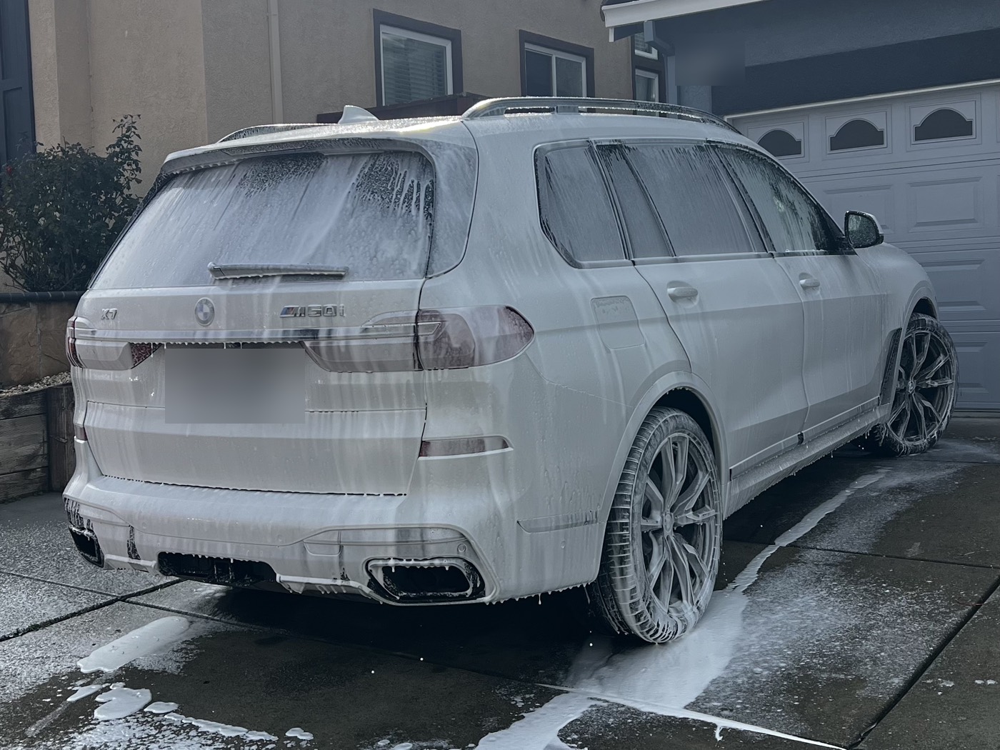 A BMW X7 under foam on a customer's driveway — Amiri's Auto Detailing working on site